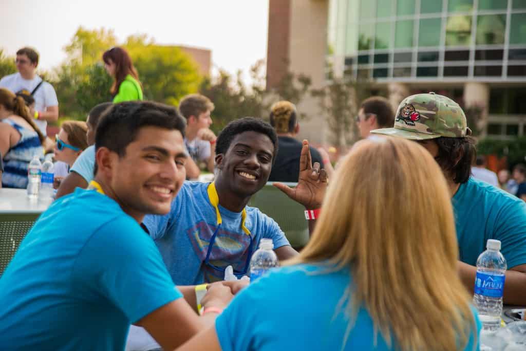 Group of students siting at table outside smiling at the camera.