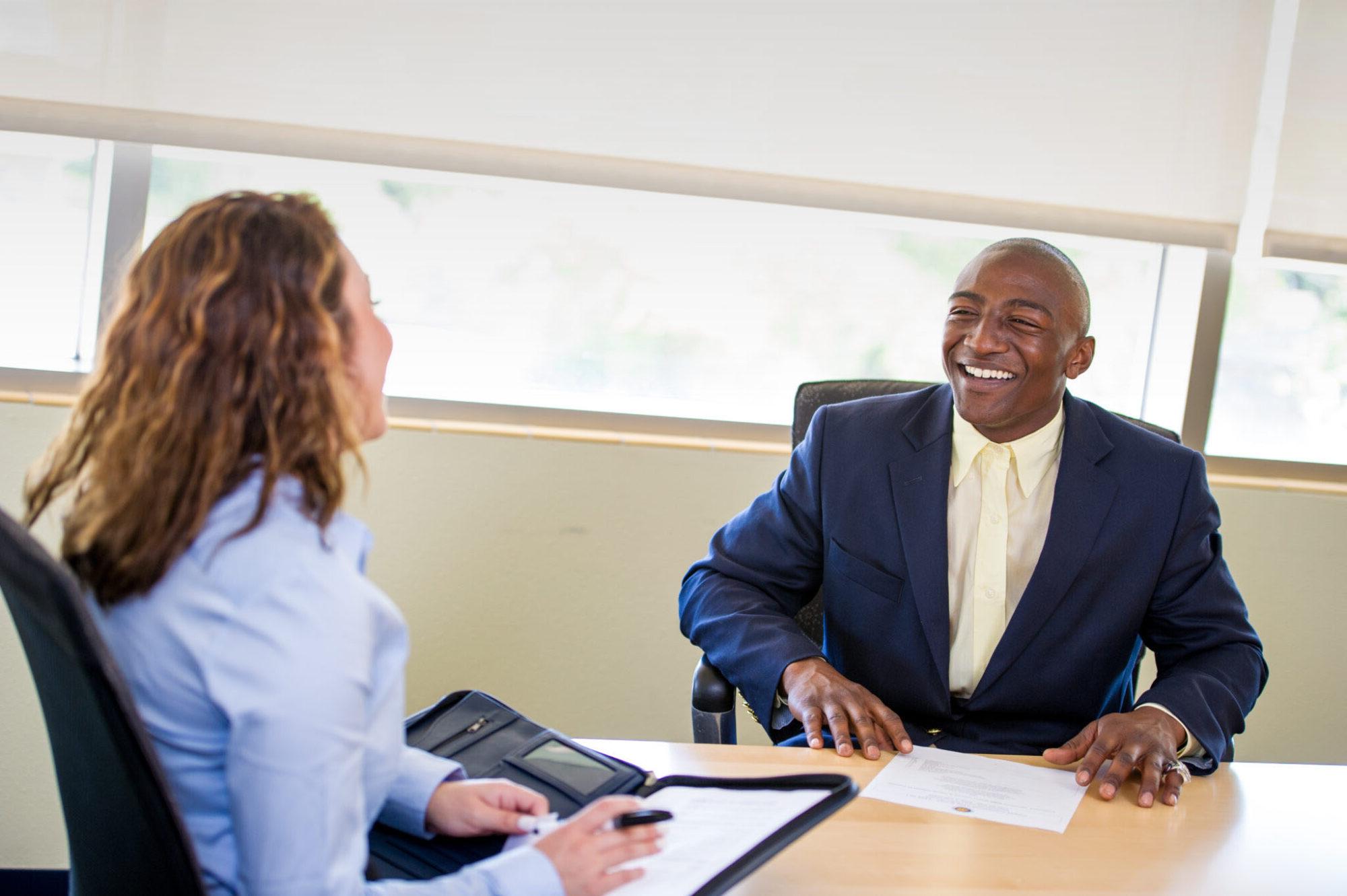 Two professionals sitting at a table speaking to each other. 