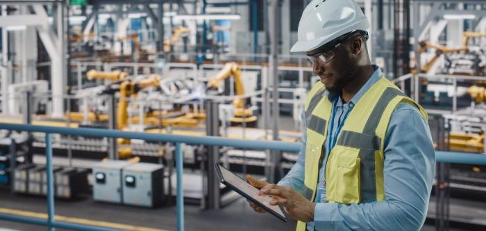 A male safety and health worker overseeing a factory assembly line.